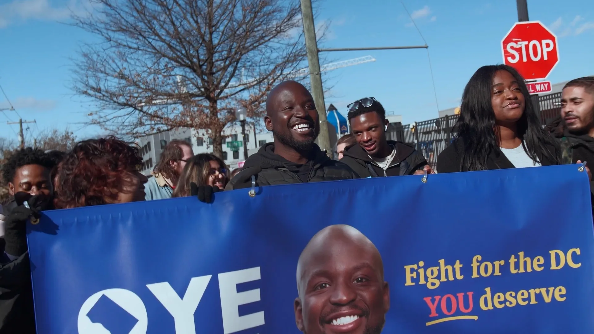 Political candidate walking with supporters and a campaign banner during an outdoor Washington, DC event.